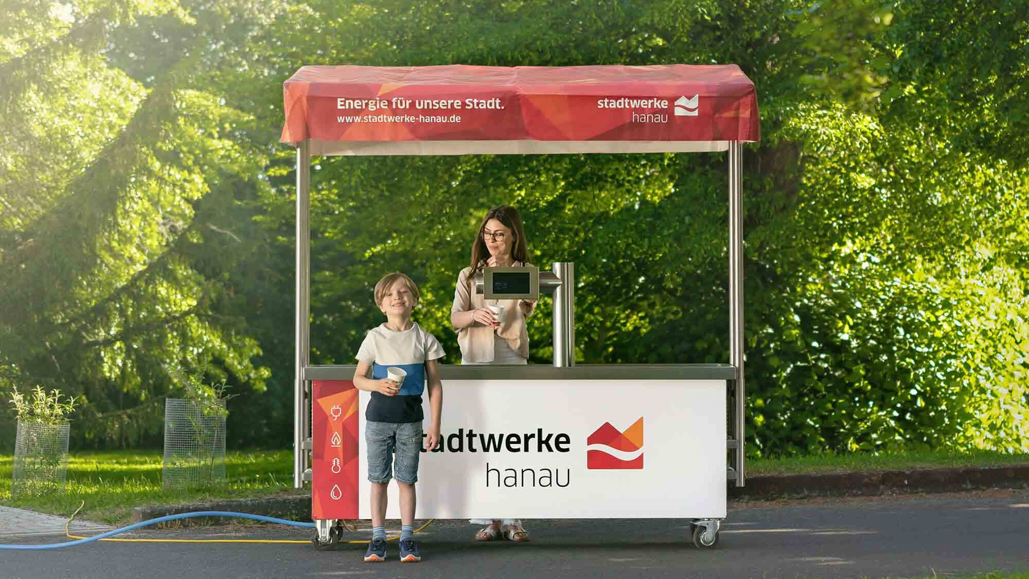 Kind steht am Trinkwasserstand der Standwerke Hanau mit einem Glas Wasser in der Hand